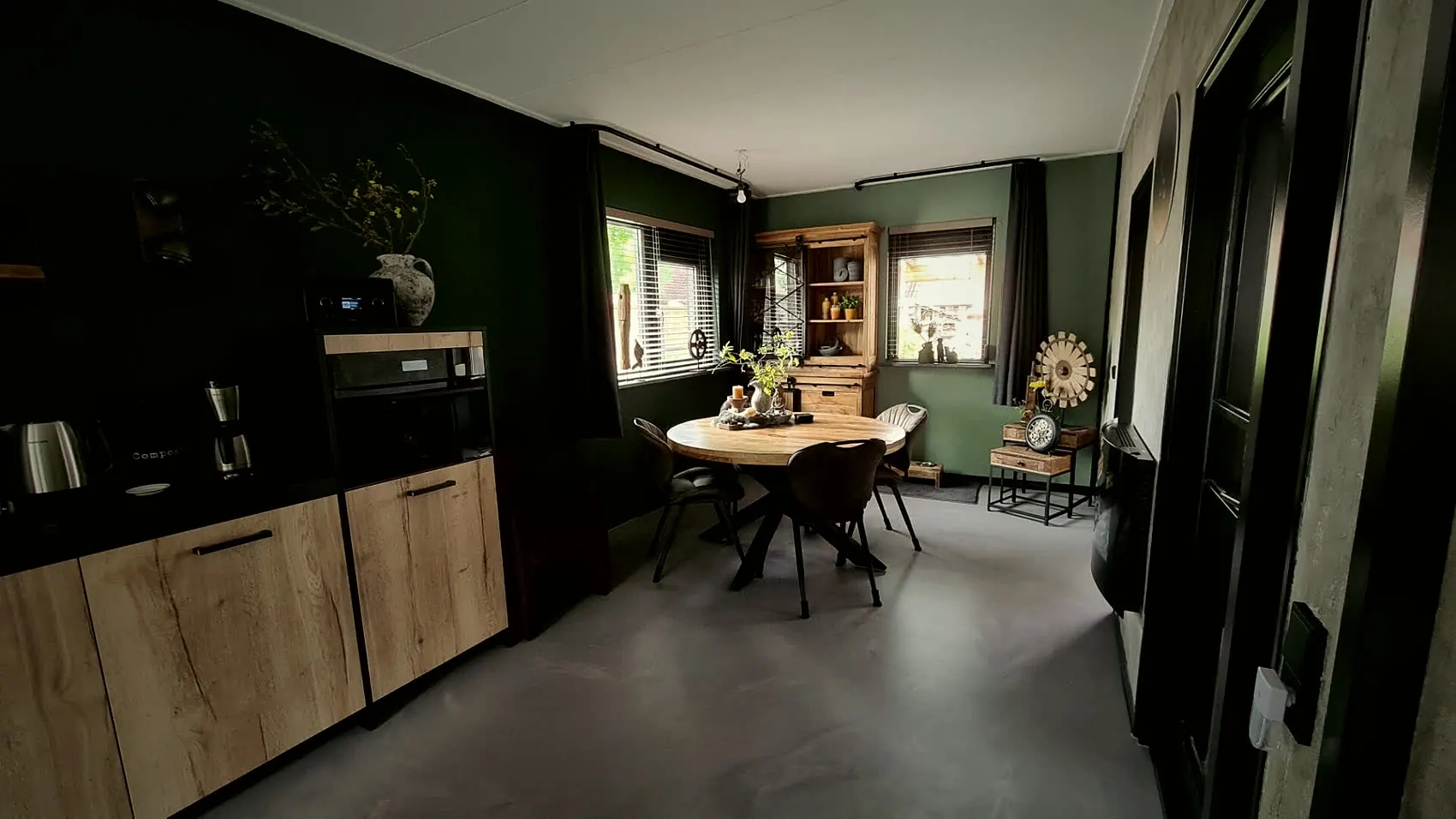 Woonkeuken met grijze gietvloer, houten keuken en donkergroene wand